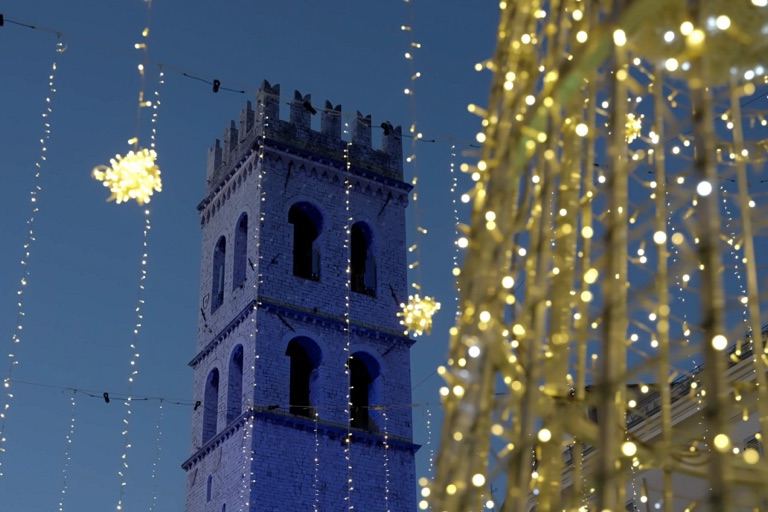 La Torre del Popolo illuminata di blu accanto all’albero di luci di Piazza del Comune ad Assisi