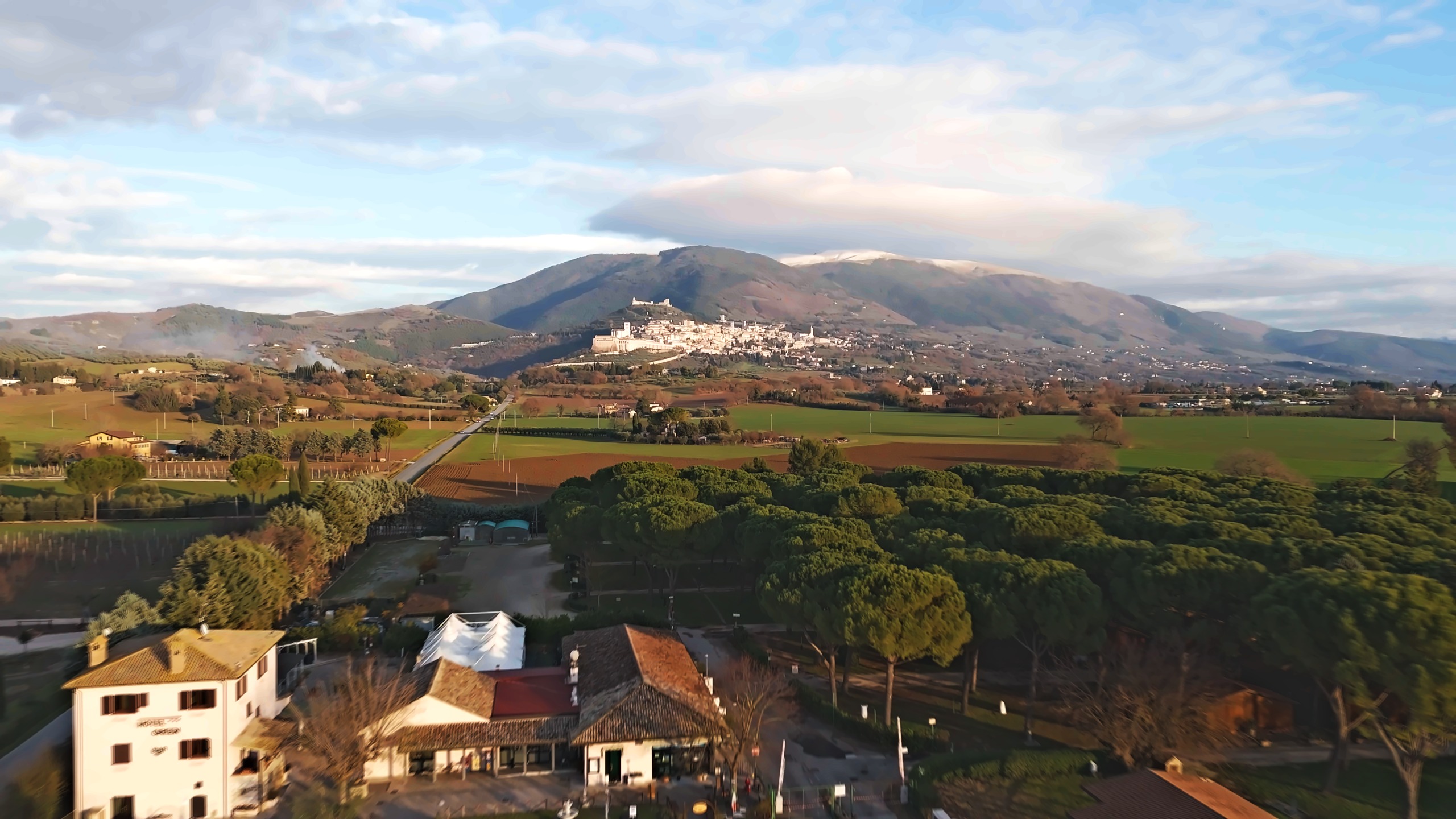 Il villaggio d'inverno visto dal drone, con la pineta, l'hotel e Assisi sotto il Monte Subasio innevato